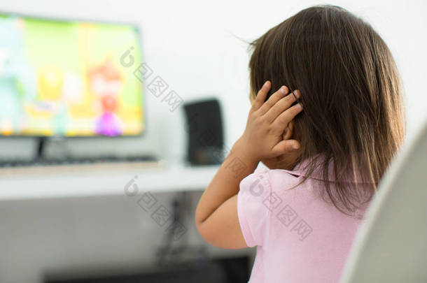 一个孩子看着电视抱着她的耳朵, 因为她害怕的声音;