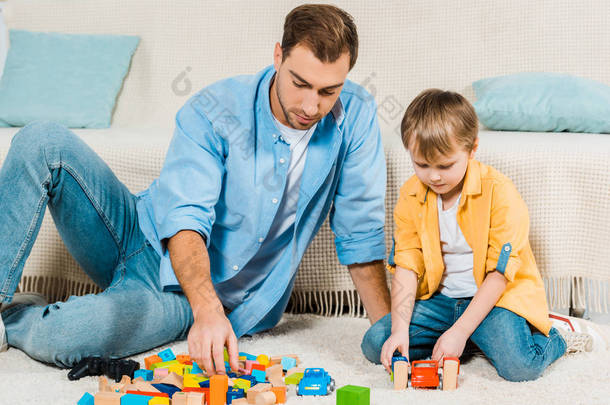 父亲和学龄前儿童的儿子玩五颜六色的积木和玩具车在家里
