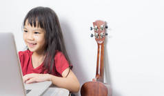 小小音乐家孩子正在她在笔记本电脑上的音乐。亚洲的孩子正在寻找音符上互联网。日本女孩正在吉他音乐课程在线.