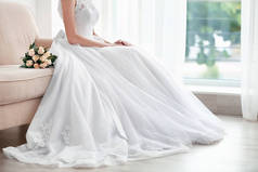新娘穿着漂亮的裙子，与坐在沙发上的婚礼花束