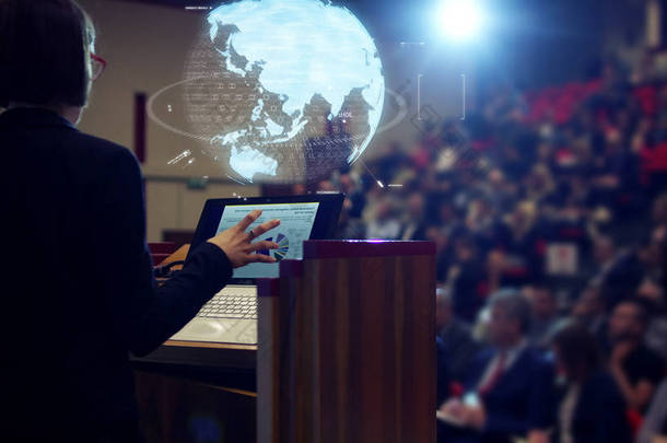 <strong>一个</strong>女人坚持经济学公约礼堂里的观众的一次演讲和资助他们 business.concept:world 经济、 未来派会议、 全息图、 技术、 商人会议