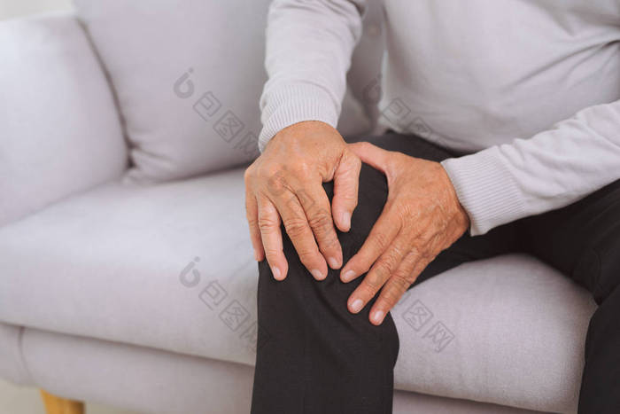坐在沙发上的老人在家里的客厅和触摸他的膝