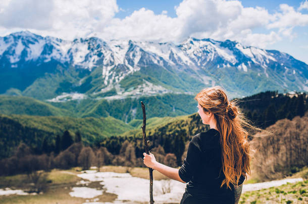 美丽的红头发女人在山坡上的山顶上多云的蓝天背景。生态旅游的概念 