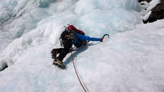 男子冰登山者在一个蓝色的夹克上一个华丽的冰冻瀑布攀登在阿尔卑斯山在深冬