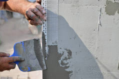 老手工工作者的手与墙壁抹灰工具整修房子。泥水匠用刮刀和石膏翻新户外墙壁和角落。墙体绝缘。建筑整理工程