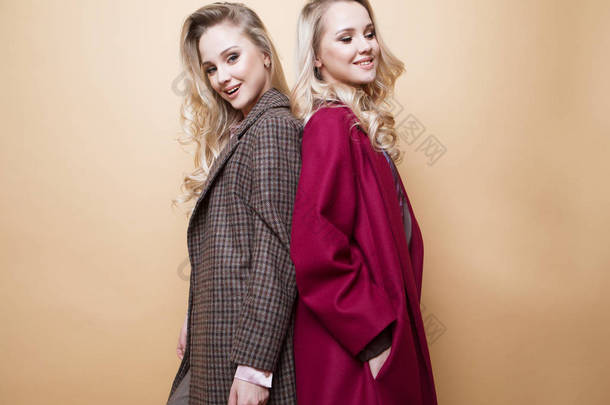  两个女孩的时尚肖像，穿着冬季时尚外套，穿着米黄色背景的衣服在室内摆姿势的<strong>最好</strong>的朋友. 