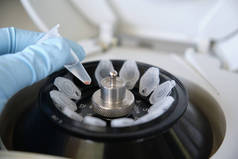 在实验室里，研究人员手拿着手套，在微型离心机上拿着一个装有弹丸的小型埃本多夫管。里面塞满了管子.