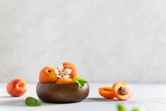 成熟的杏仁和杏仁叶子在白色混凝土背景的木制碗里。侧视图,复制文本的空间.有机水果。食谱，市场横幅