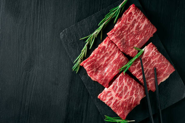在<strong>黑色背景</strong>的盘子里，切碎的牛扒牛肉，优质的日本肉和木棍，顶部视图和复制的空间