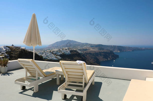 <strong>甲板</strong>椅和雨伞在豪华度假酒店的阳台上海景。希腊圣托里尼岛露台的椅白色建筑.