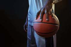 强壮的篮球手手拿球在演播室里,黑色背景.职业男篮手，穿着运动服打体育比赛，高个子运动员