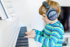 漂亮的小小孩男孩戴着耳机在客厅或音乐学校钢琴。学龄前儿童开心学习演奏乐器。教育，技能的概念
