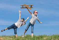 两个小孩白天在公园里玩纸板玩具飞机。快乐游戏的概念。孩子们在外面玩得很开心在蓝天的背景上拍摄的图片.