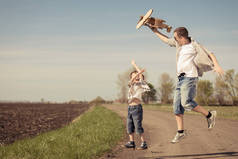爸爸和儿子白天在公园里玩纸板玩具飞机。友好家庭的概念。人们在户外玩得很开心在蓝天的背景上拍摄的图片.