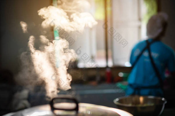 当厨师工作时，一个巨大的电饭锅在食堂里<strong>沸腾</strong>，其晨光反射出大量的蒸汽.