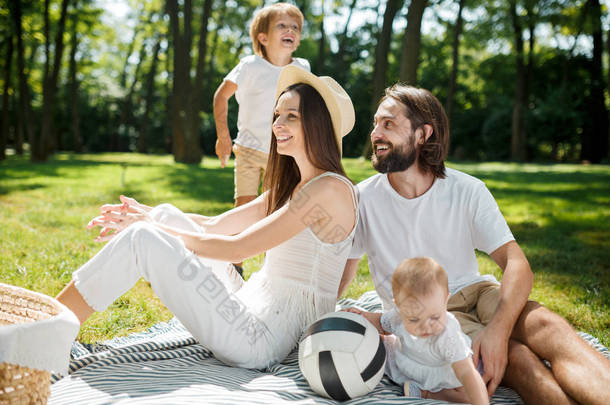 母亲、父亲、儿子和小女儿, 穿着白色衣服, 在公园里野餐休息。幸福的家庭.