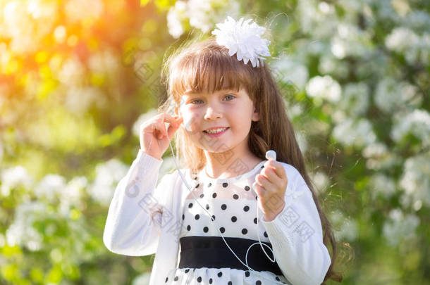 小女孩在白色礼服听<strong>录音</strong>在耳机在夏天和公园。女孩从她的手机听音乐.