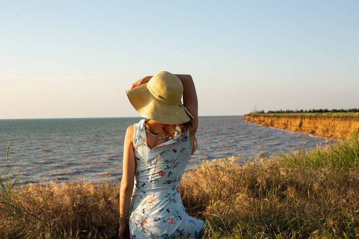 年轻的浪漫妇女穿着蓝色的礼服和帽子在背景