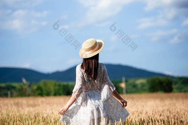 一个女孩从背后在麦田里的画像一个穿着白衣、头戴帽子的漂亮姑娘在麦田里的画像。穿白衣戴白帽的女孩。麦田.
