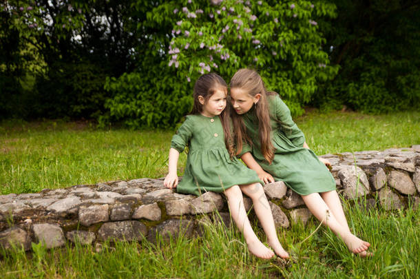 两个身穿绿色亚麻布衣服的姐姐，在公园里欢度着盛开的紫丁香，享受着春天和温暖。美丽的春天花园。快乐的童年家庭、爱情、和平与<strong>幸福</strong>概念