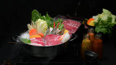 背景为黑色的火锅、鲜切肉、海味食品和蔬菜、日本火锅风格的火锅中的火锅的近景 