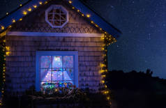 灯光下的童话般的房子和一个发光的窗户, 有一棵圣诞树和一个星空。夜景.