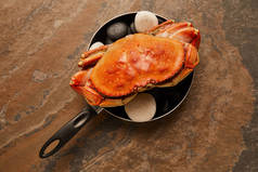 在纹理表面的煎锅中，未煮熟的螃蟹与实心壳与黑色石头的顶视图