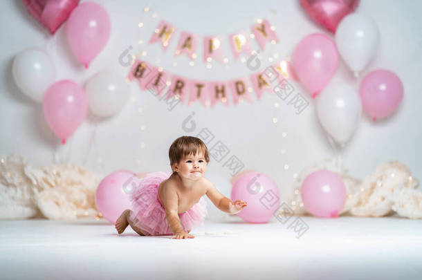 大年初一，一个穿着粉红短裙的快乐小女孩爬上背景，带着花环和粉红气球，庆祝她的第一个生日。生日装饰.