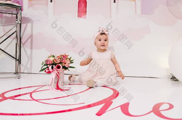一个小女孩的画像，她有一束花，背景很浅。穿着粉红衣服的小奢侈品公主生日庆祝的概念是一年。一个坐在地板上玩耍的孩子.