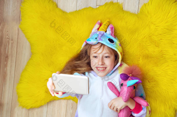 穿着独角兽睡衣、头戴玩具的可爱女孩会自作主张，躺在地板上玩乐。顶部视图