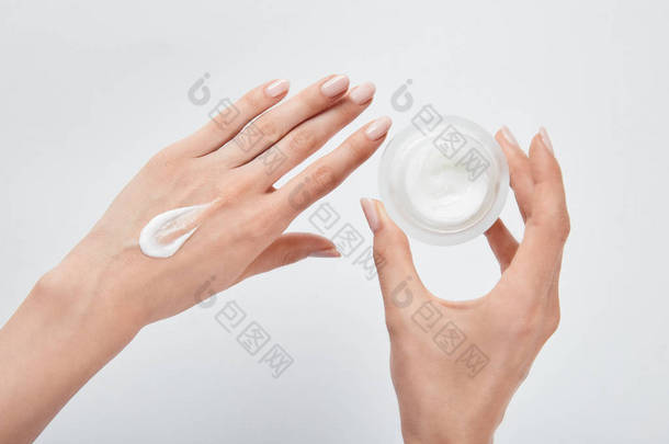 裁剪视图的妇女涂霜在皮肤上，并持有罐子隔离在白色
