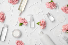 白色背景上不同化妆品瓶、康乃馨花、棉棒和化妆品垫的顶视图