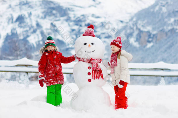 小孩堆雪人孩子们造雪人。在寒冷的冬日，男孩和女孩在户外玩耍。家家户户在山里过圣诞假期很开心.孩子们在瑞士山区玩耍.