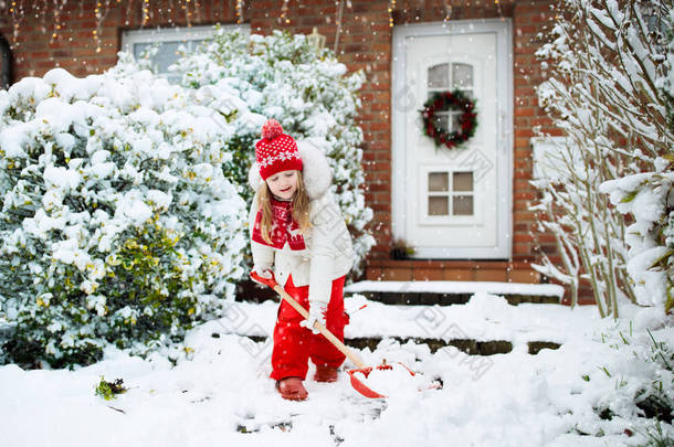 孩子们铲雪。冬天暴风雪过后，一个拿着铲子的小女孩正在清理车道。圣诞节暴风雪过后,孩子们清空了家门口的小路.降雪的乐趣。孩子们在冰冷寒冷的花园里玩耍.