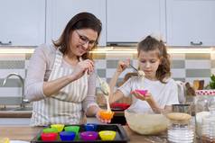 妈妈和女儿在家里厨房一起做松饼.将生面团倒入硅胶模中的母子.母亲节、家庭、自制烘焙健康食品