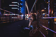 女用膝上型电脑耳机听音乐的侧面在城市街道上的夜晚