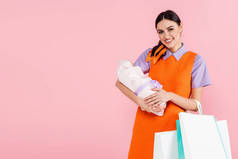 快乐的女人拿着刚出生的孩子和粉色购物袋对着相机微笑