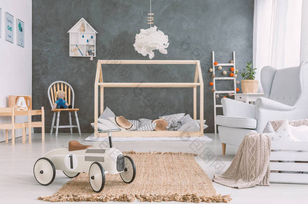 汽车玩具在地毯旁边的扶手椅在灰色的孩子的卧室内部与木床。真实照片
