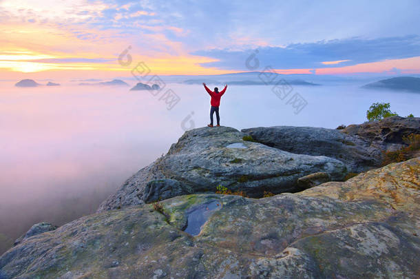 锋利的岩石峰上的后方人剪影。满足的徒步旅行者欣赏的景色。高个子男人在悬崖上
