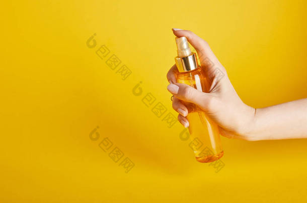 在黄色背景的<strong>喷雾</strong>瓶中，妇女拿着<strong>防晒</strong>油的裁剪视图