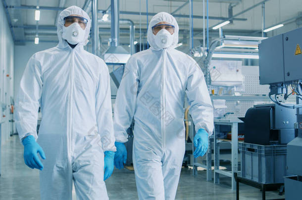 两名工程师/科学家在危险品无菌西装步行通过技术先进的工厂/实验室。用 Cnc 机械清洁高科技环境.