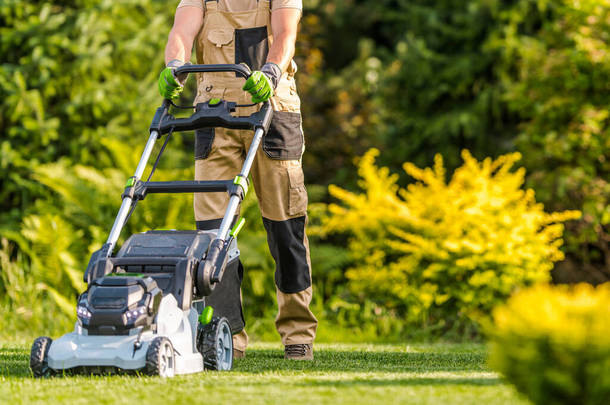 40多岁的白人花园工人在大后院花园用现代电动无绳割草机割草。园林绿化产业主题.