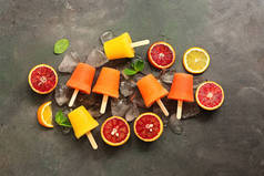 用柑橘、薄荷和冰块在深色的乡村背景上对橙子进行分类。用红色和黄色的橙子冻在手杖上.俯瞰，平铺