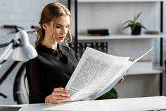 专注的女商人在黑色正式服装坐在办公桌和阅读报纸在工作场所