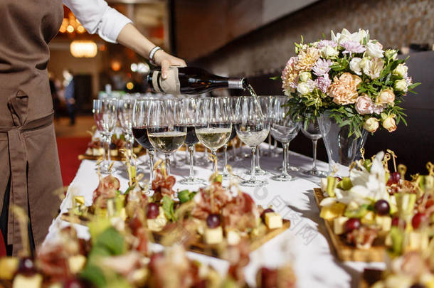 酒保将香槟或葡萄酒倒入餐厅餐桌上的酒杯中。隆重举行的婚礼或新年快乐晚宴
