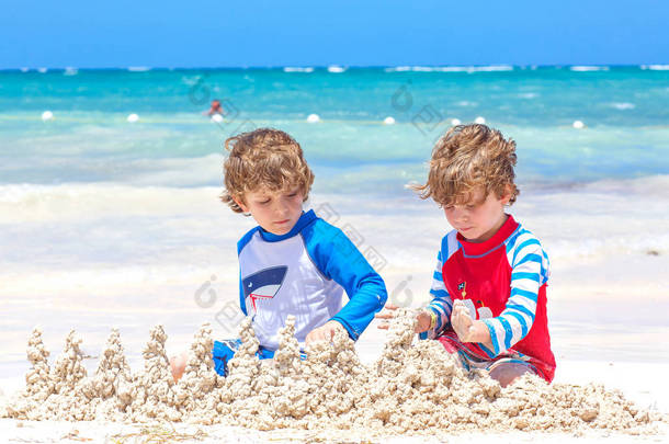 两个小男孩在岛上的热带海滩上建造一个沙堡，玩得很开心。健康的孩子在度假时一起玩耍。孪生<strong>兄弟</strong>，快乐的<strong>兄弟</strong>们笑着