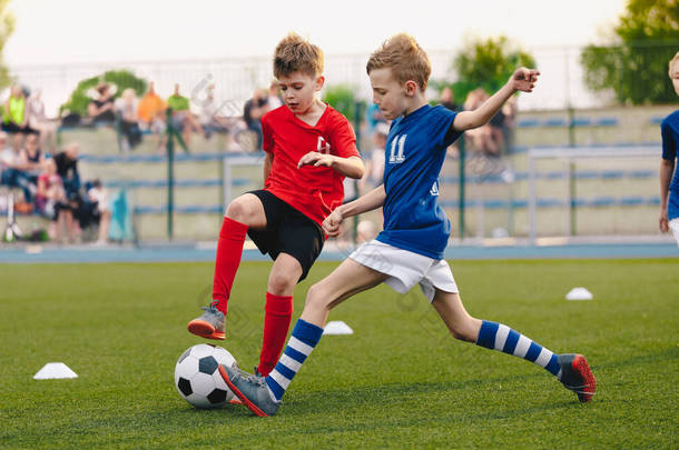 儿童足球运动员在足球场上踢球。体育足球横向背景。观众在后台体育场<strong>观看</strong>。身穿红衣和蓝衣的青少年运动员。体育教育