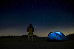夜间拍摄，背景是深蓝色的天空和星星- -旅行和自由的概念，帐篷在野外野外野营- -站着观看周围的风景