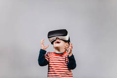 兴奋的孩子有乐趣与 vr 眼镜。在灰色背景下佩戴虚拟现实耳机的开朗儿童的肖像.