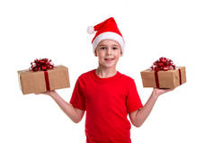 帅气快乐的男孩, 头上戴着圣诞老人的帽子, 手上有两个礼品盒, 直视镜头。概念: 圣诞节或新年快乐假期